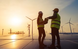 Auf dem Bild sind zwei Personen zu sehen. Im Hintergrund sind Windräder und solaranalogen zu sehen.