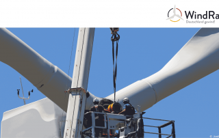 Menschen mit einem Kran auf Höhe eines Windrads bei Bauarbeiten, die Repowering symbolisieren.