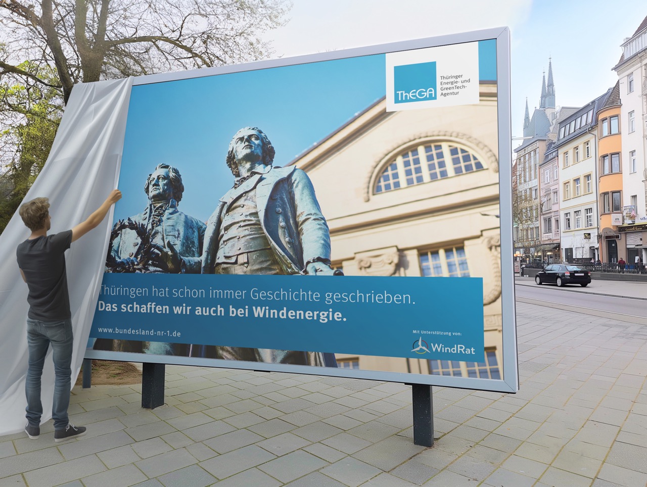 Man sieht einen Mann, der ein Plakat für mehr Windenergie in Thüringen enthüllt.