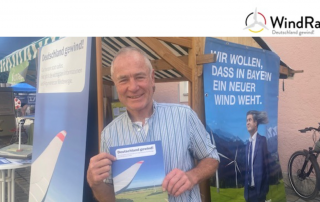 Auf dem Bild ist Peter Keller zu sehen, wie er am Stand des Windrats zum Klimatag in Murnau die Windrat Broschüre hochhält.