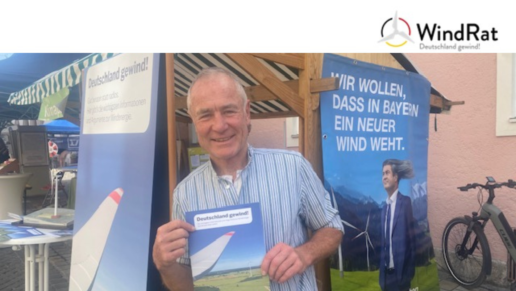 Auf dem Bild ist Peter Keller zu sehen, wie er am Stand des Windrats zum Klimatag in Murnau die Windrat Broschüre hochhält.