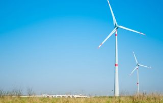 Man sieht zwei Windräder auf einer Wiese vor blauem Himmel als Symbolbild für den Windenergieausbau in Deutschland.